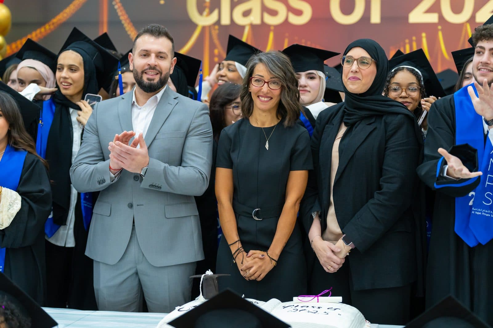 ANPS staff and the graduating Class of 2025 gathered together in caps and gowns, smiling around a Class of 2025 celebration cake