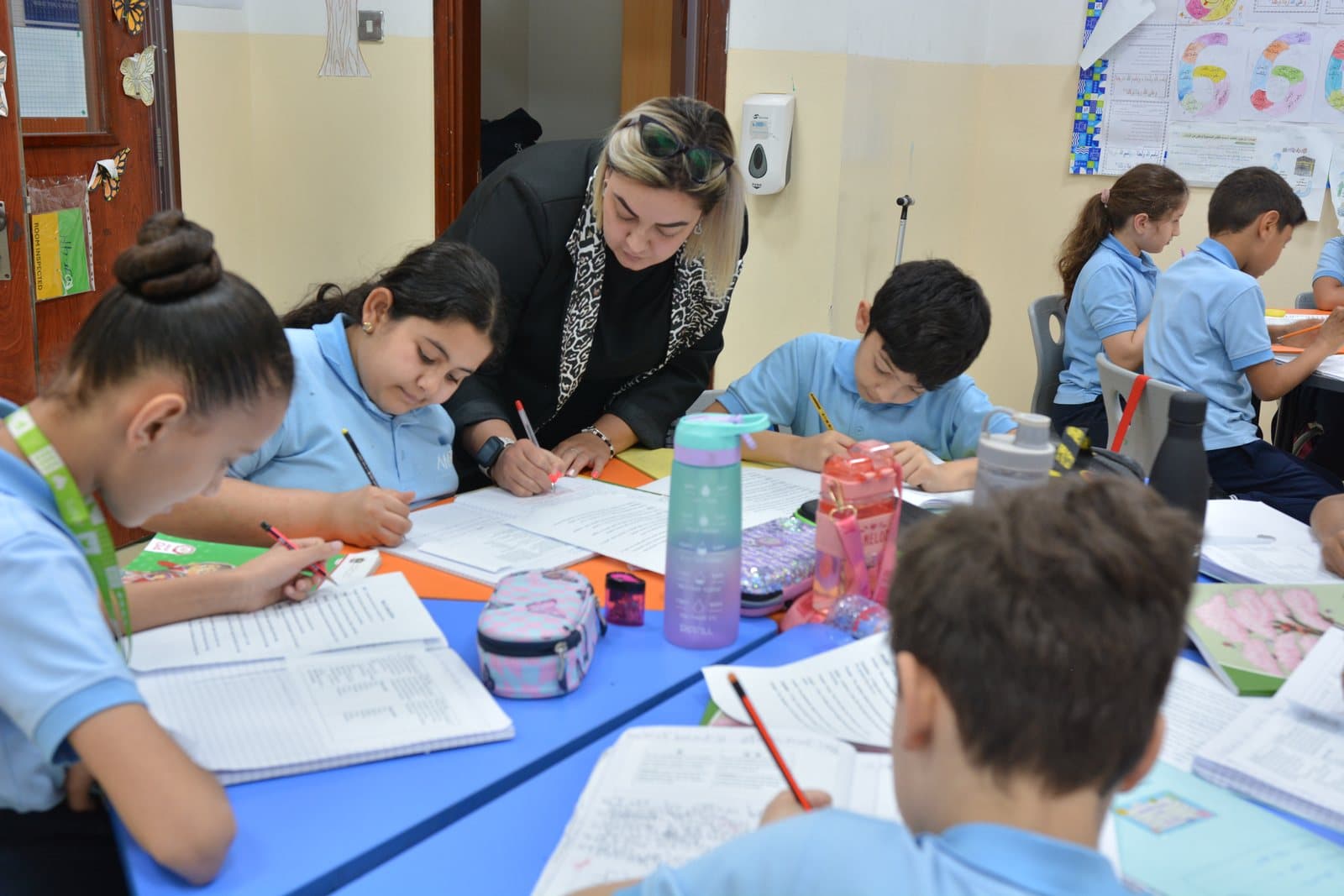An Al Najah Private School teacher supporting students at their desks in a busy classroom