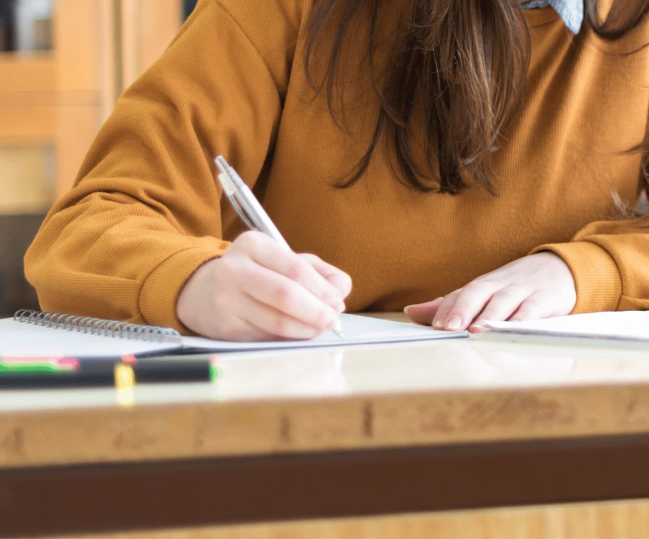 An Al Najah Private School student writing in a notebook during an IGCSE lesson